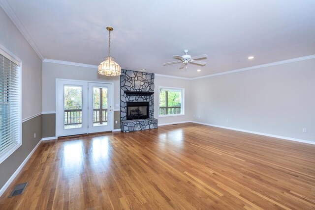 unfurnished living room with ornamental molding, hardwood / wood-style floors, ceiling fan with notable chandelier, and a stone fireplace