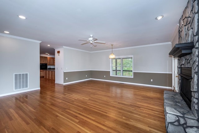 unfurnished living room with a stone fireplace, dark hardwood / wood-style flooring, ornamental molding, and ceiling fan