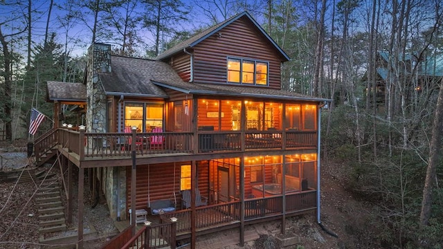 back house at dusk with a sunroom and a wooden deck