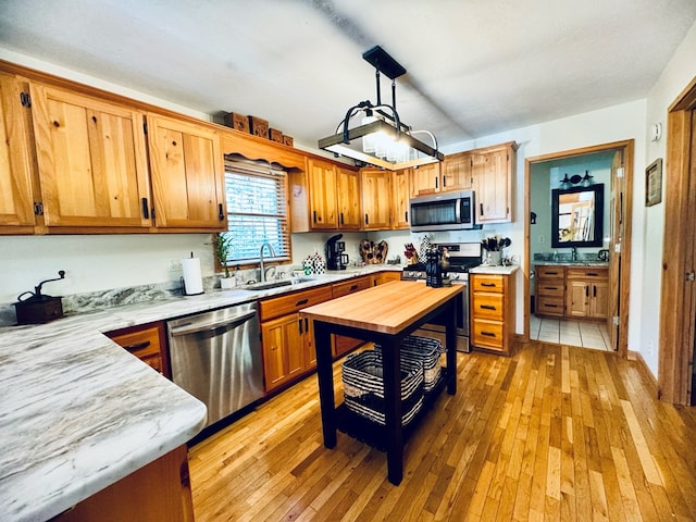 kitchen with appliances with stainless steel finishes, hanging light fixtures, butcher block counters, light hardwood / wood-style floors, and sink