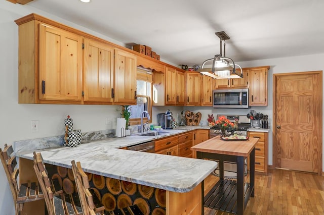 kitchen featuring appliances with stainless steel finishes, decorative light fixtures, sink, light wood-type flooring, and kitchen peninsula