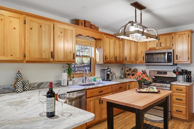 kitchen with appliances with stainless steel finishes, light hardwood / wood-style flooring, hanging light fixtures, light stone counters, and sink