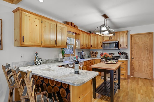 kitchen featuring pendant lighting, light hardwood / wood-style floors, stainless steel appliances, light brown cabinetry, and kitchen peninsula