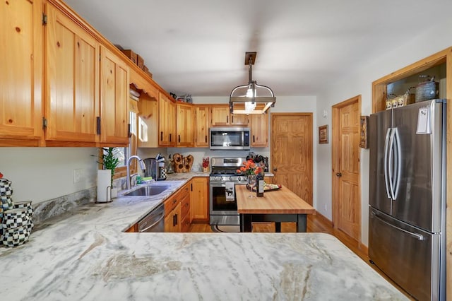 kitchen with appliances with stainless steel finishes, sink, light stone counters, and decorative light fixtures