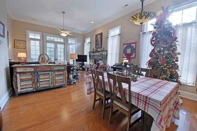 dining room with a fireplace, wood-type flooring, ceiling fan, crown molding, and french doors