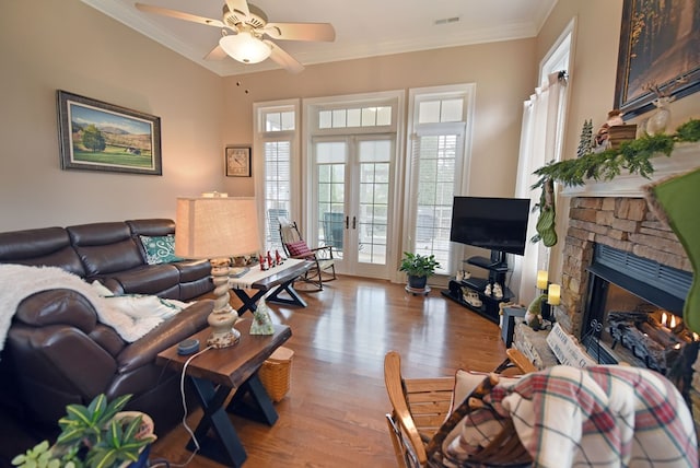 living room with a stone fireplace, ceiling fan, light hardwood / wood-style floors, crown molding, and french doors