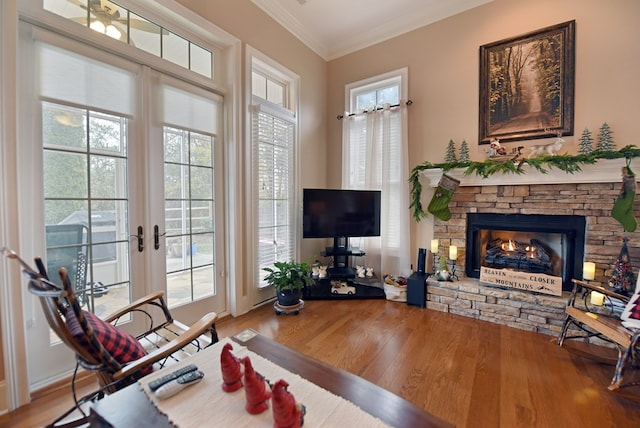 living room featuring hardwood / wood-style flooring, ornamental molding, a stone fireplace, and french doors