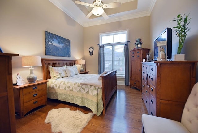 bedroom with crown molding, dark wood-type flooring, a raised ceiling, and ceiling fan