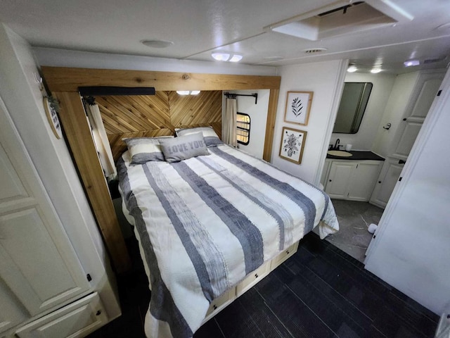 bedroom featuring ensuite bath, hardwood / wood-style flooring, sink, and wooden walls