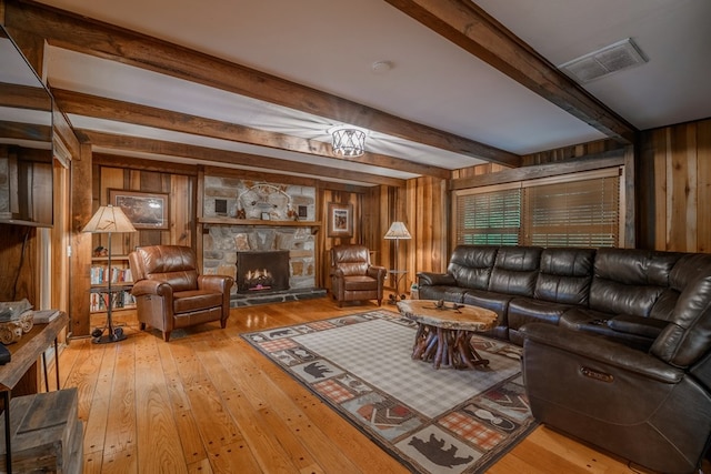 living room featuring wooden walls, beam ceiling, hardwood / wood-style flooring, and a stone fireplace