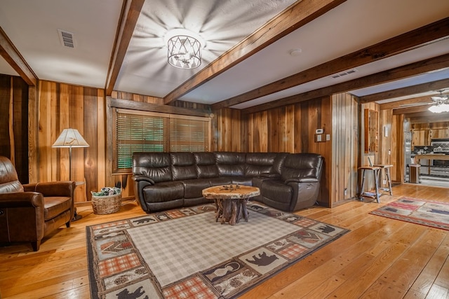 living room with beamed ceiling, wooden walls, light hardwood / wood-style flooring, and ceiling fan