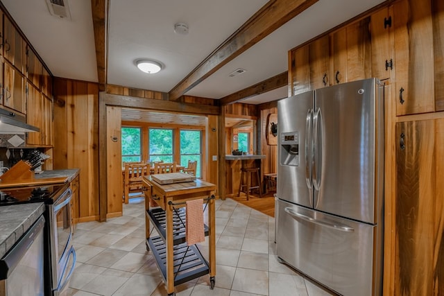 kitchen featuring beamed ceiling, appliances with stainless steel finishes, and light tile flooring