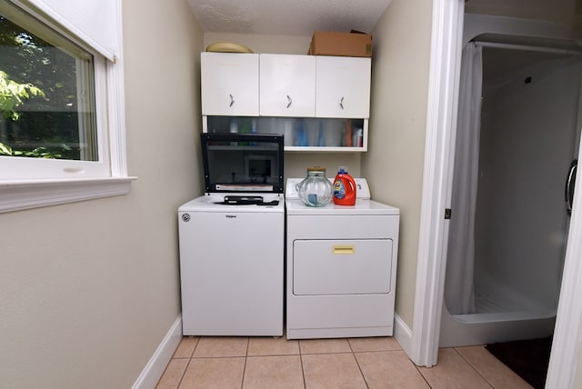 laundry area featuring washer and clothes dryer, light tile patterned floors, cabinets, and a textured ceiling