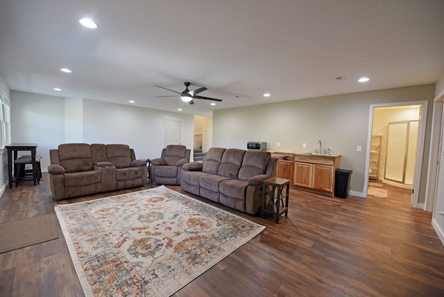 living room with a textured ceiling, ceiling fan, dark wood-type flooring, and sink