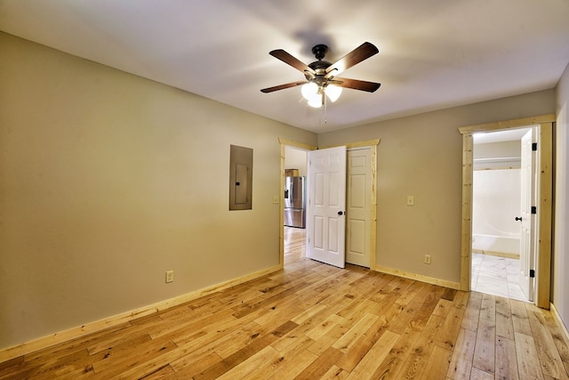 unfurnished bedroom with connected bathroom, electric panel, ceiling fan, light hardwood / wood-style floors, and stainless steel refrigerator with ice dispenser