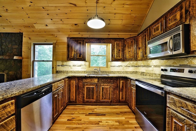 kitchen with sink, appliances with stainless steel finishes, pendant lighting, light stone countertops, and light hardwood / wood-style floors