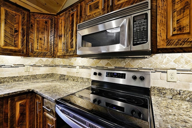 kitchen featuring lofted ceiling, light stone countertops, decorative backsplash, and stainless steel appliances