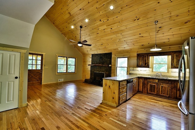 kitchen with a stone fireplace, kitchen peninsula, pendant lighting, stainless steel appliances, and light stone countertops