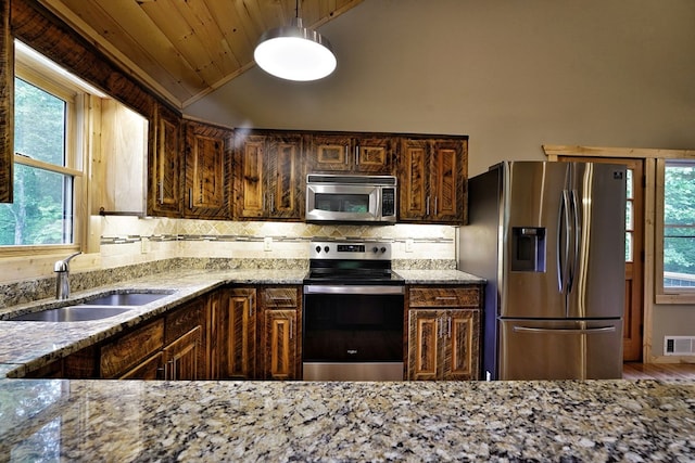 kitchen with sink, hanging light fixtures, stainless steel appliances, decorative backsplash, and vaulted ceiling