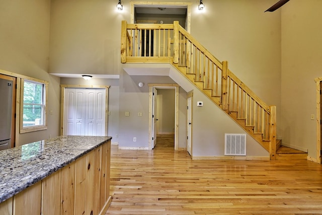 kitchen featuring a towering ceiling, light brown cabinetry, light stone countertops, and light hardwood / wood-style flooring