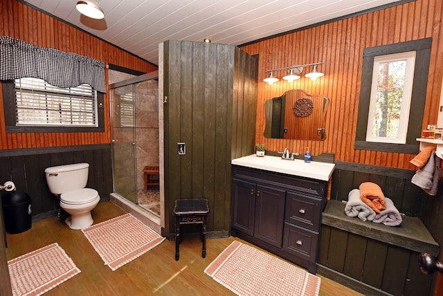 bathroom with wood-type flooring, vanity, wooden walls, toilet, and a shower with shower door