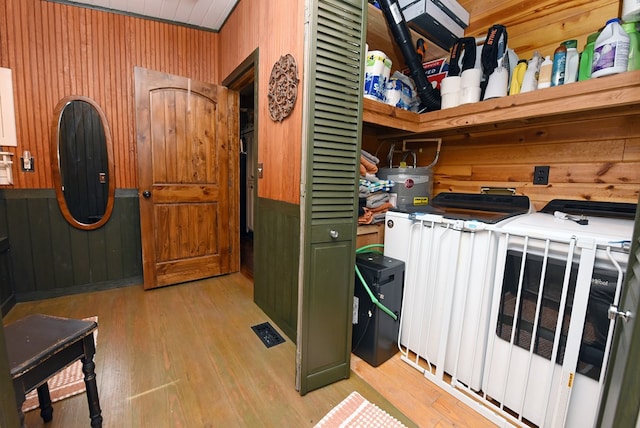 clothes washing area featuring water heater, wood walls, light wood-type flooring, and washer / dryer