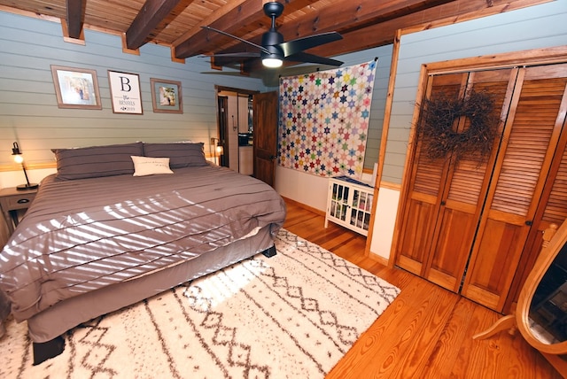 bedroom with wood walls, wooden ceiling, beamed ceiling, ceiling fan, and light wood-type flooring