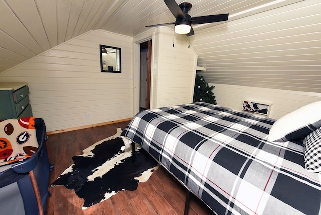 bedroom with ceiling fan, dark hardwood / wood-style floors, wood walls, and vaulted ceiling