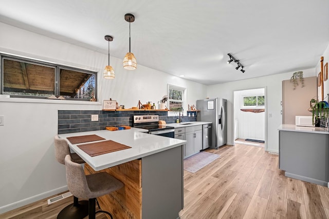 kitchen with a kitchen breakfast bar, decorative backsplash, stainless steel appliances, light countertops, and a peninsula