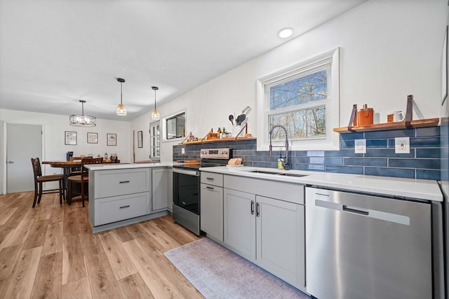 kitchen featuring an inviting chandelier, open shelves, a sink, a peninsula, and appliances with stainless steel finishes