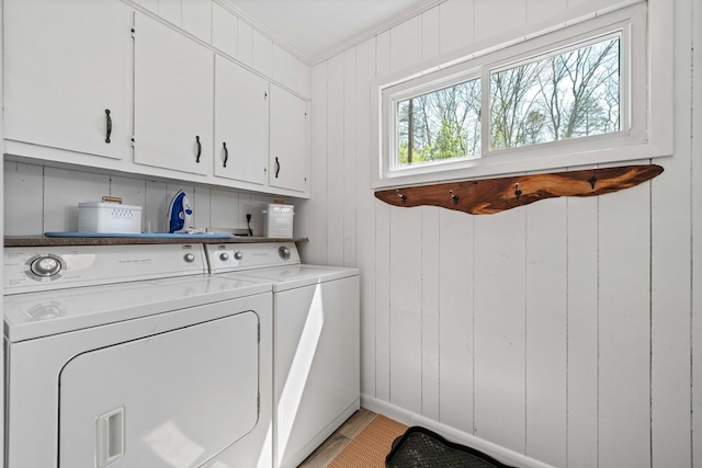 washroom with cabinet space, light wood-type flooring, ornamental molding, and washer and clothes dryer