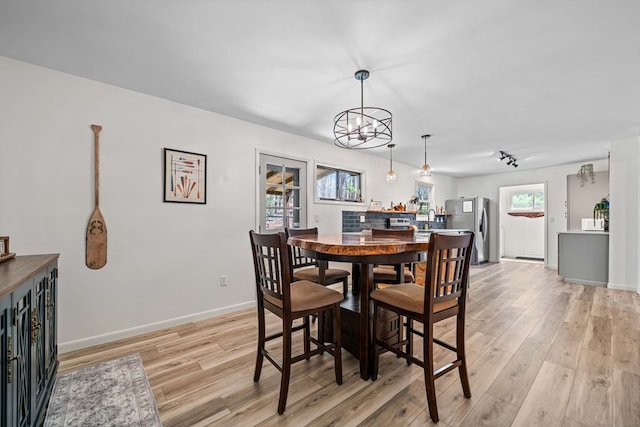 dining space with light wood-type flooring, baseboards, rail lighting, and a notable chandelier