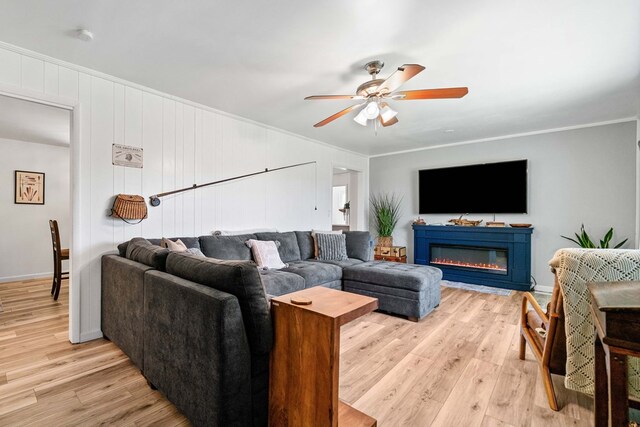living area featuring ceiling fan, ornamental molding, a glass covered fireplace, and light wood-type flooring