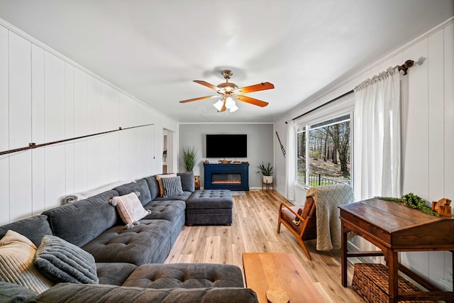 living room featuring crown molding, a glass covered fireplace, light wood finished floors, and a ceiling fan