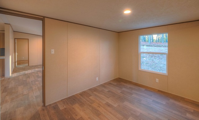 empty room with hardwood / wood-style floors, a textured ceiling, and vaulted ceiling