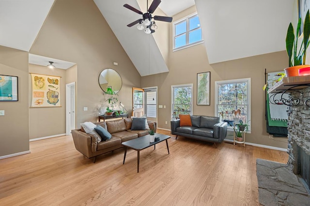 living room with high vaulted ceiling, ceiling fan, a stone fireplace, and light hardwood / wood-style floors