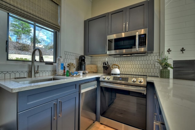 kitchen with light wood-type flooring, tasteful backsplash, stainless steel appliances, sink, and light stone countertops