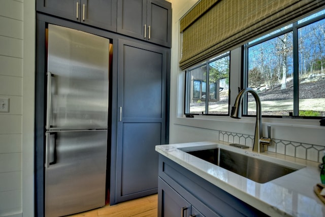 kitchen featuring high quality fridge, light stone countertops, light hardwood / wood-style floors, and sink