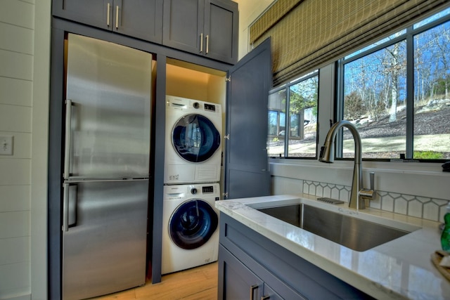 laundry room with stacked washer and dryer, sink, and light hardwood / wood-style floors