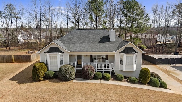 single story home with covered porch, a shingled roof, a chimney, and fence