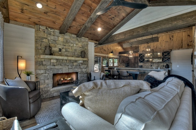 living room featuring ceiling fan with notable chandelier, a stone fireplace, wood ceiling, wooden walls, and vaulted ceiling with beams