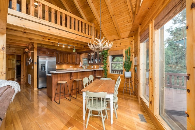 dining area with high vaulted ceiling, wood walls, light wood-type flooring, wooden ceiling, and beam ceiling