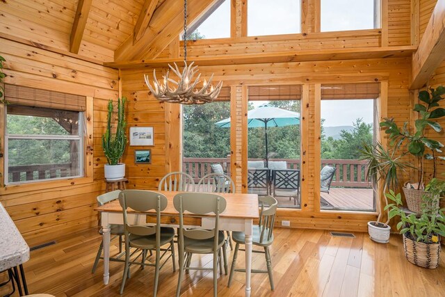 dining area featuring beam ceiling, a stone fireplace, wooden walls, an inviting chandelier, and light hardwood / wood-style floors