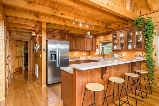 kitchen with beamed ceiling, kitchen peninsula, light hardwood / wood-style flooring, wooden walls, and stainless steel fridge