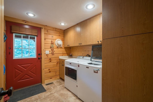 washroom with cabinets, wooden walls, and washer and dryer