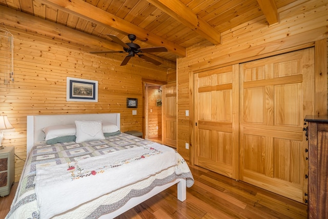 bedroom with wood walls, ceiling fan, beamed ceiling, and hardwood / wood-style flooring