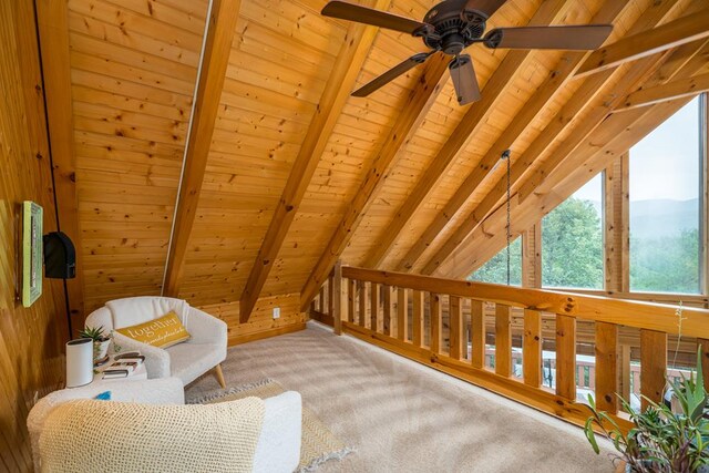 living area with ceiling fan, vaulted ceiling with beams, wooden walls, carpet, and wooden ceiling