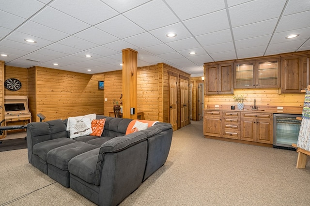 carpeted living room with beverage cooler, wood walls, and sink