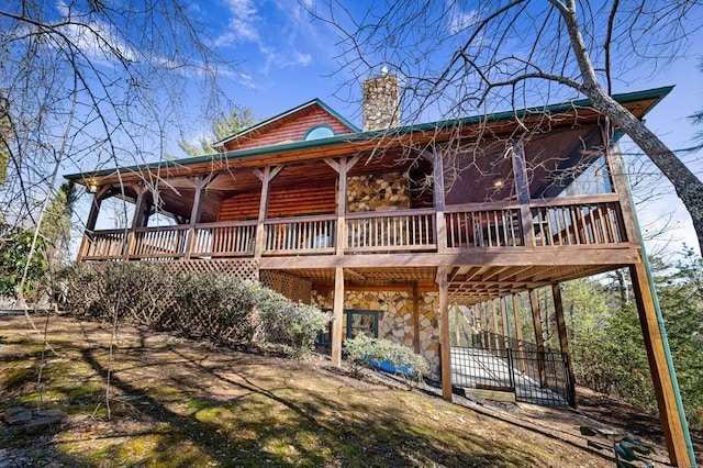 rear view of house featuring stone siding, a chimney, and a deck