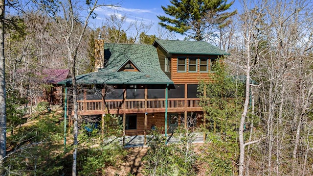 back of property featuring a shingled roof, faux log siding, a sunroom, and a chimney